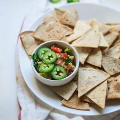 Tortilla chips with with small bowl full of spicies on white plate
