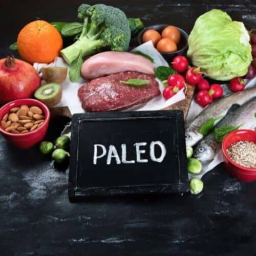 vegetables, meats, fruits and small table with Paelo sign on black background