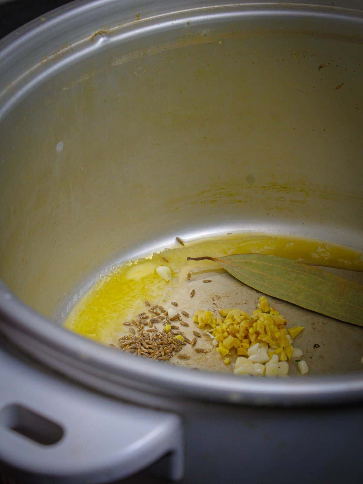 Add butter, cumin seeds, garlic, ginger, and bay leaf in a pot and saute.