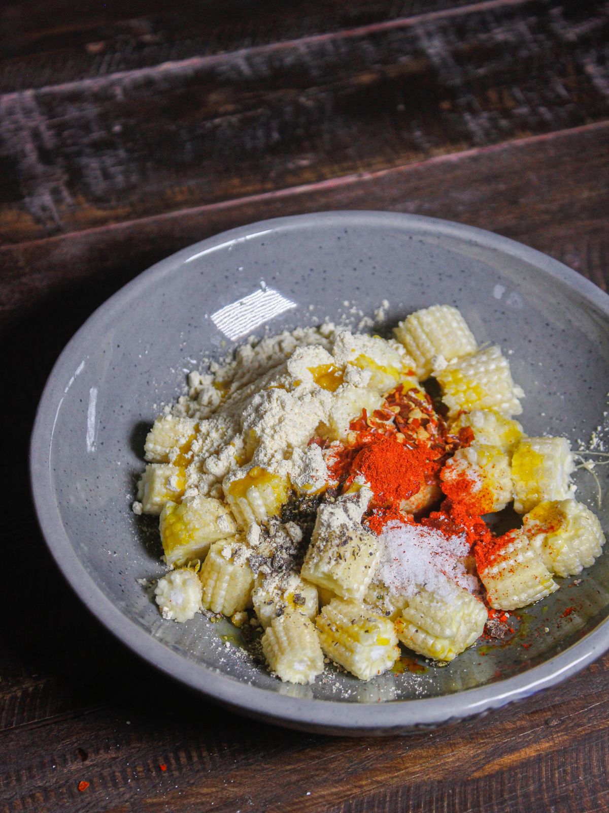 Take baby corn and add powdered spices and chickpea flour on a plate  