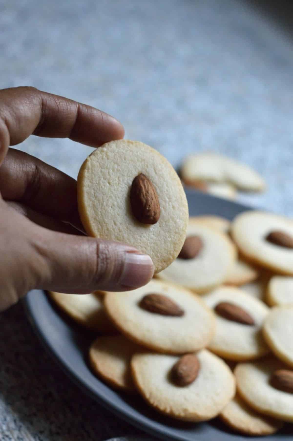 Badam Cookie held by hand over a tray full of cookies.