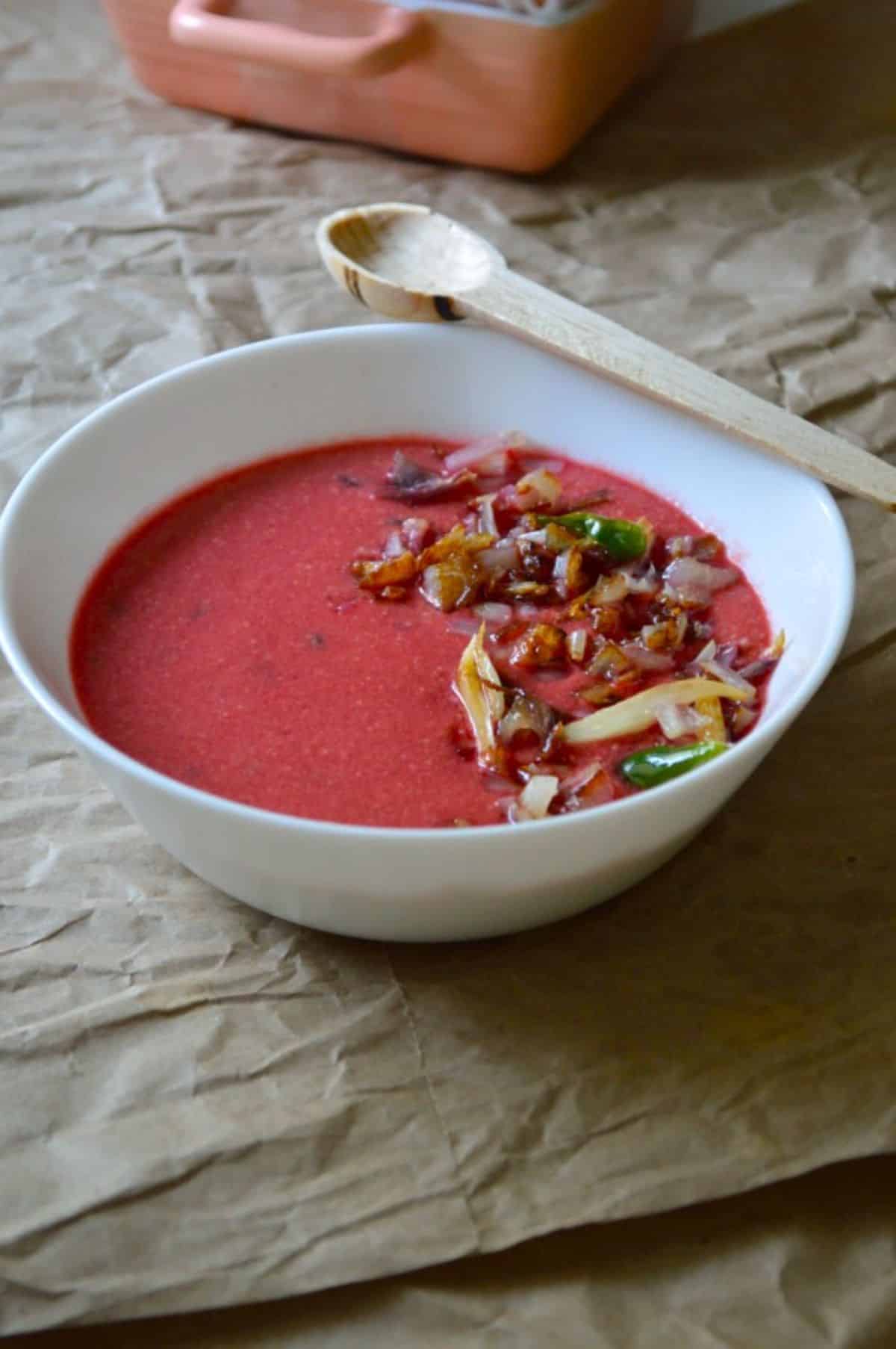Beetroot Kadhi dish in a white bowl with a wooden spoon.