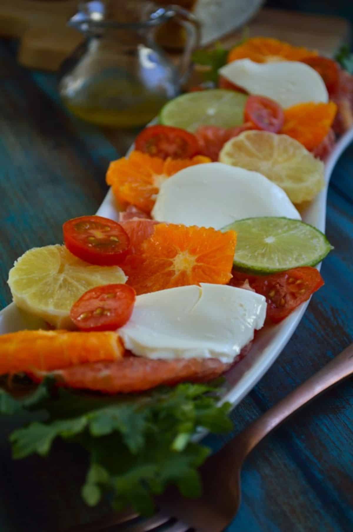 Citrus Caprese Salad on a white tray on a blue wooden table.