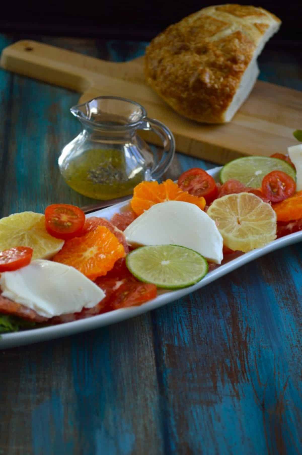 Citrus Caprese Salad on a white tray on a blue wooden table.