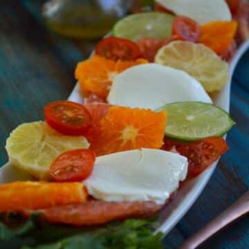 Citrus Caprese Salad on a white tray on a blue wooden table.