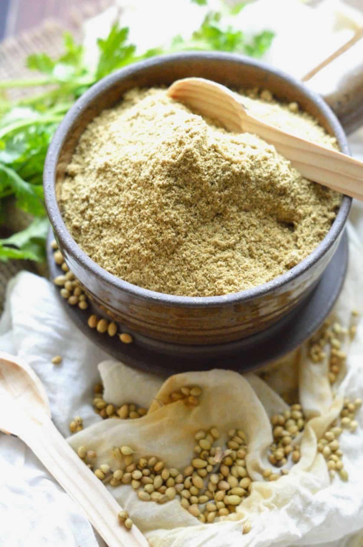 Coriander Powder in a brown bowl with a wooden spoon.