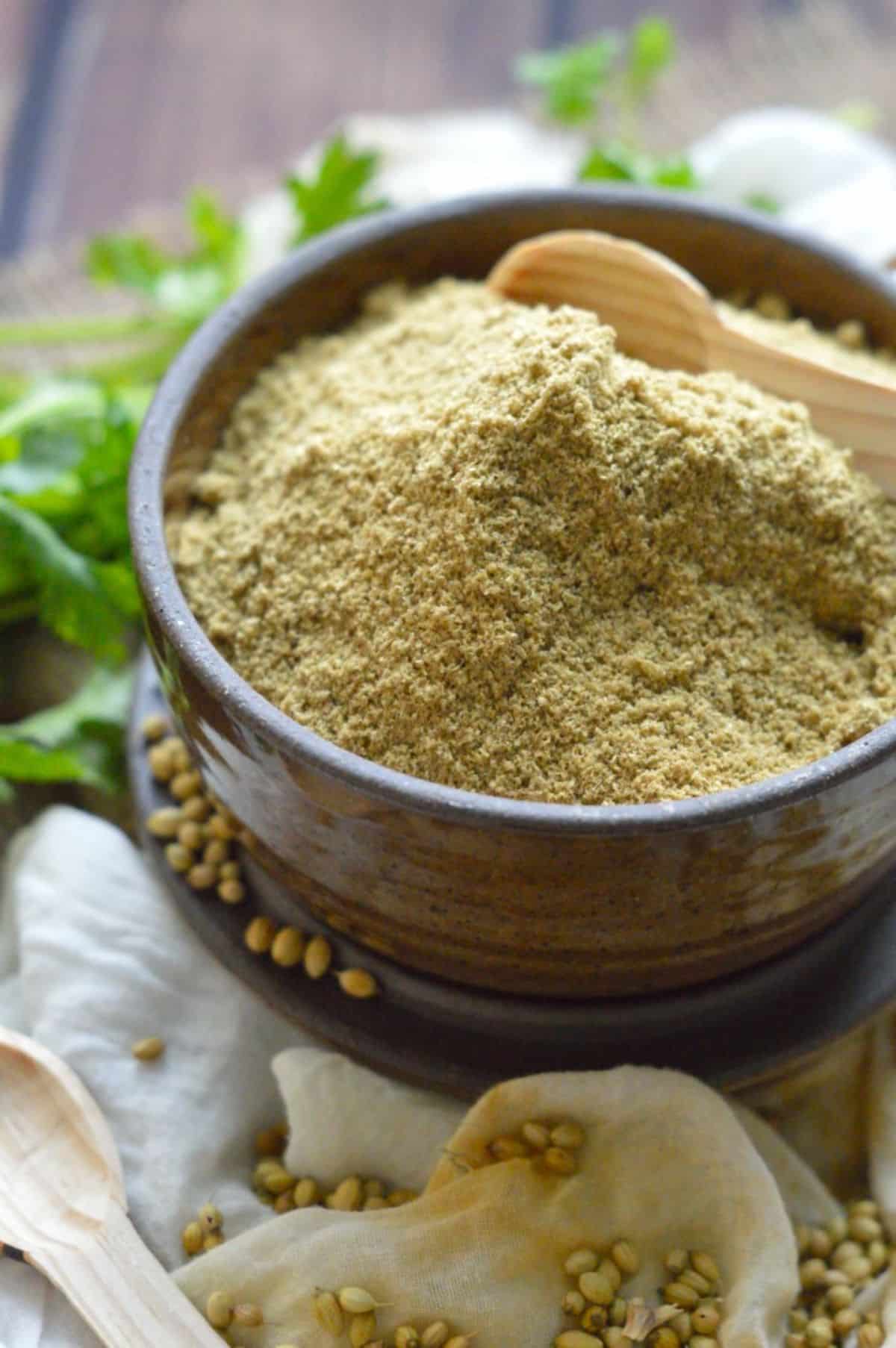 Coriander Powder in a brown bowl with a wooden spoon.