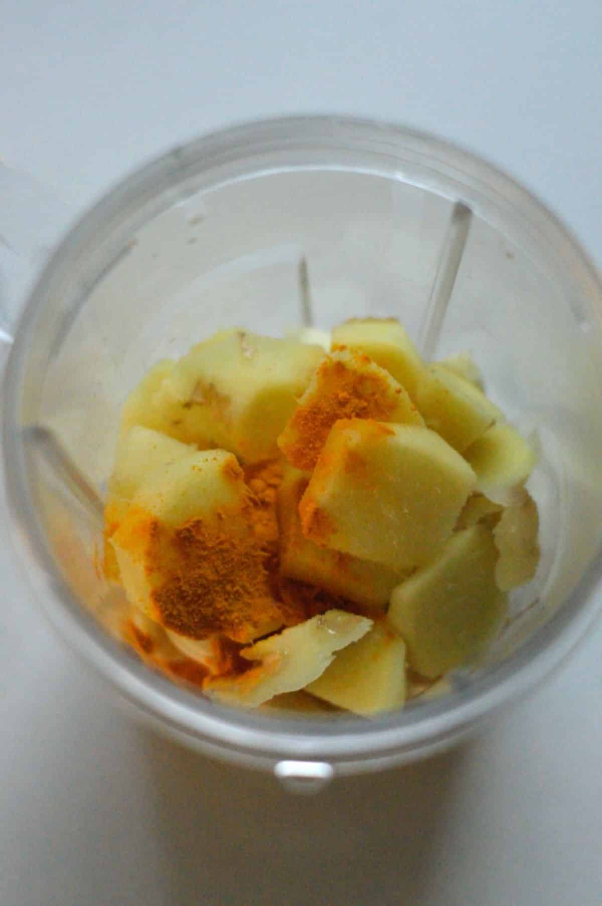 Sliced ginger root and peeled garlic cloved spinkled with turmeric powder in a blender.