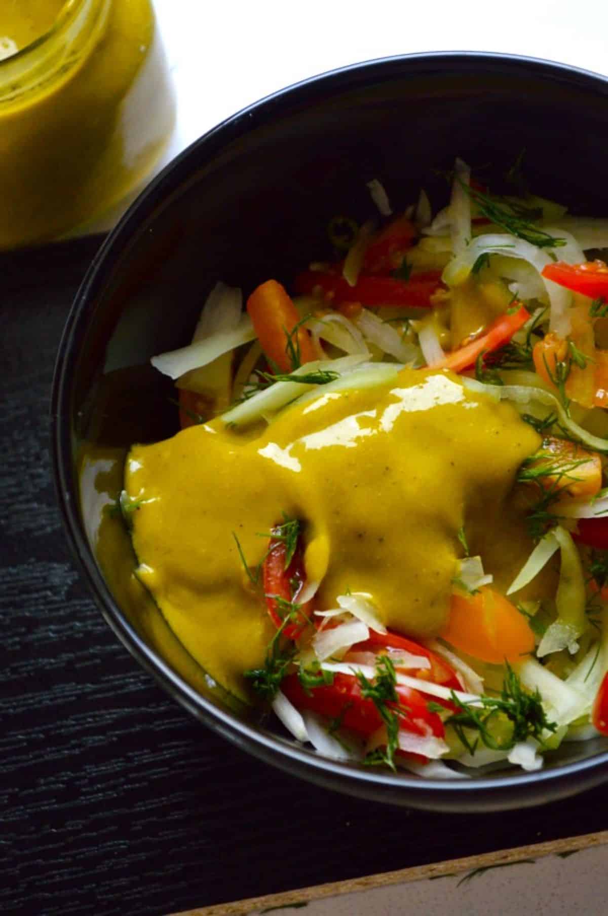 Vegan Green Papaya Salad in a black bowl drizzled with a spicy mango dressing.