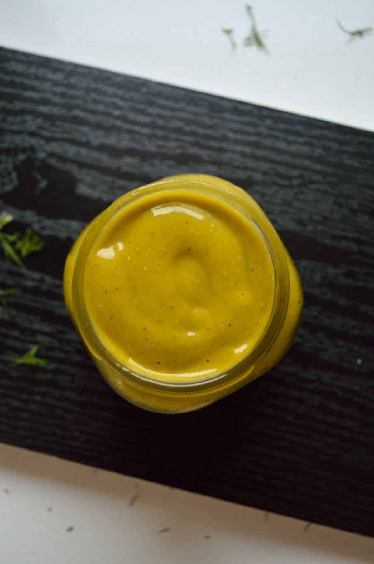 Jar of a spicy mango dressing on a wooden tray.