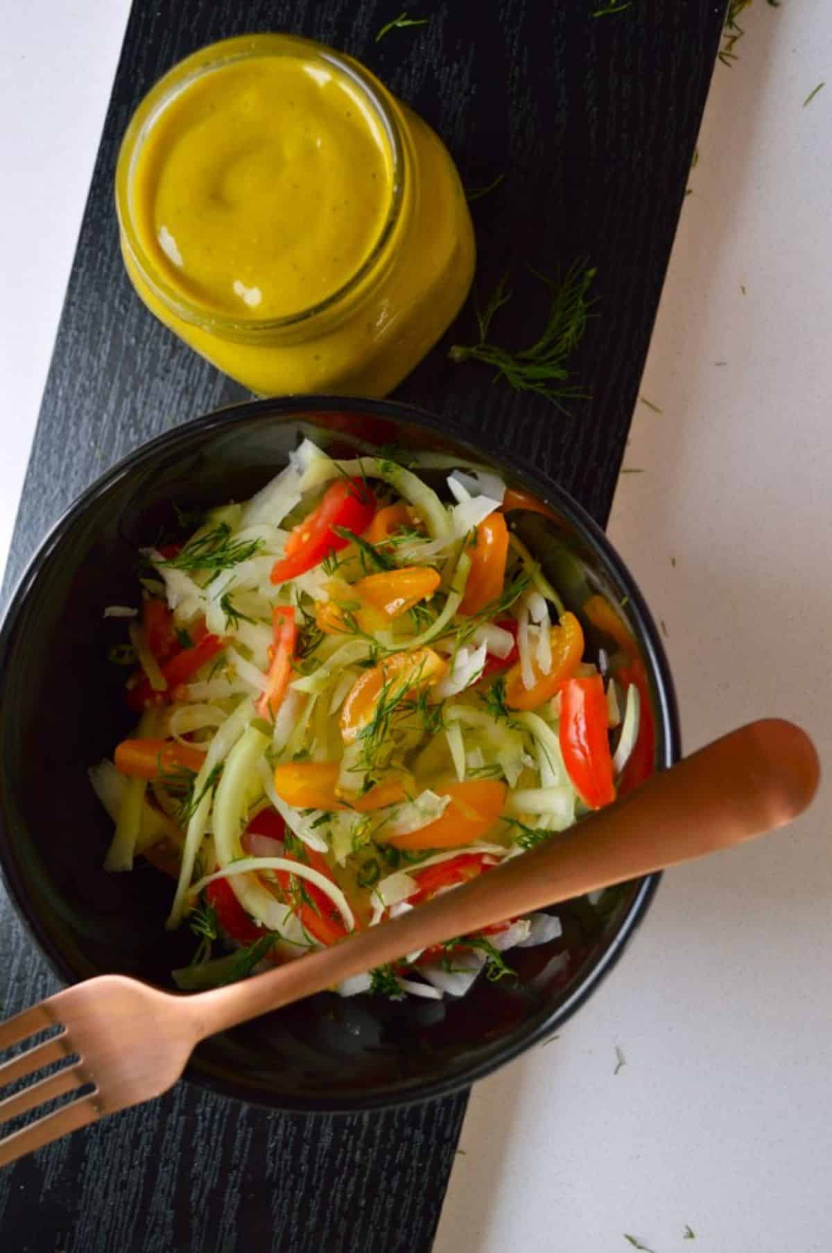 Vegan Green Papaya Salad in a black bowl with a fork  on a wooden tray.