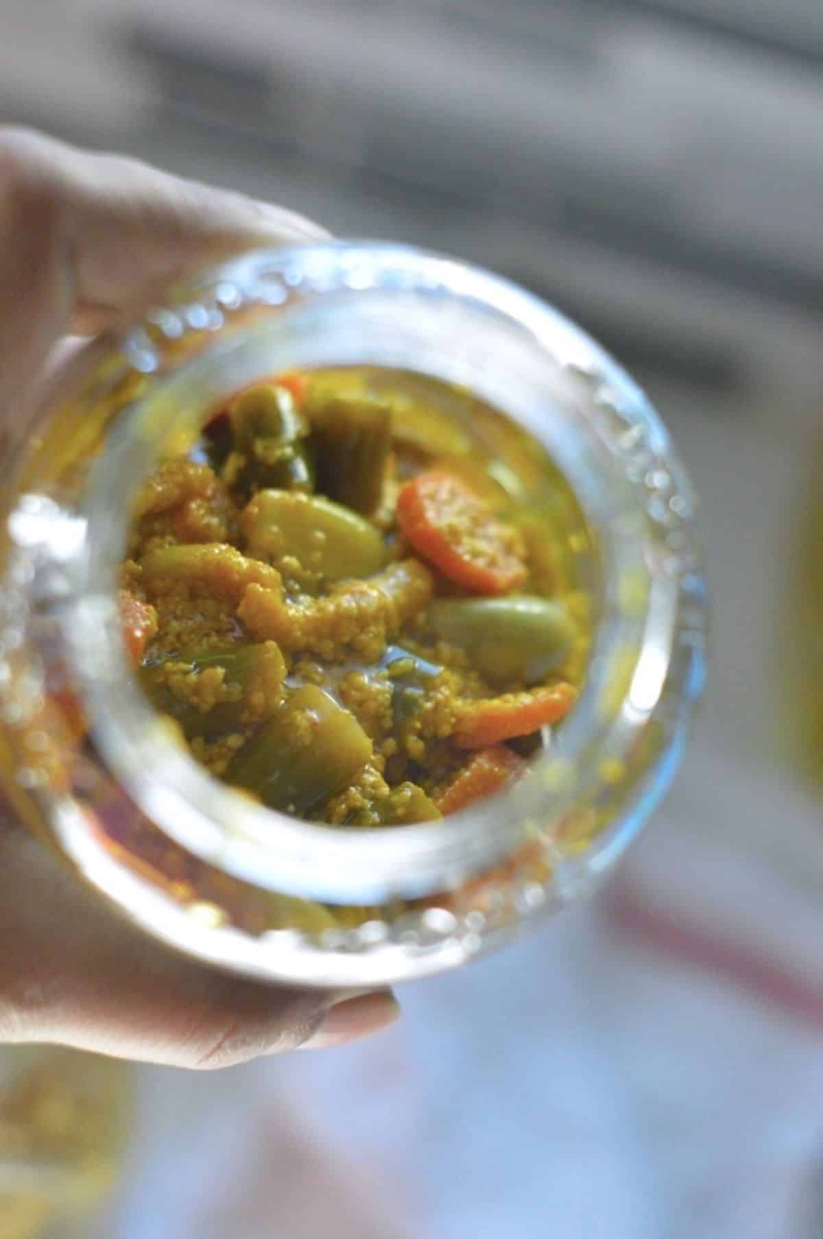 Indian Mixed Pickle in a glass jar held by hand.
