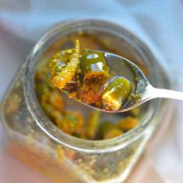Indian Mixed Pickles in a glass jar with a spoon..