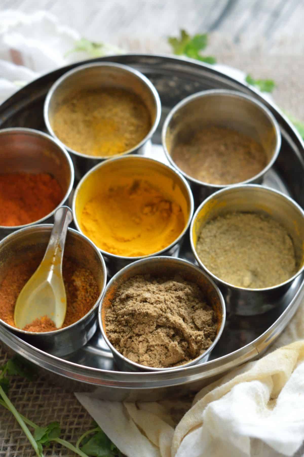 7 different spices in bowls on a tray.