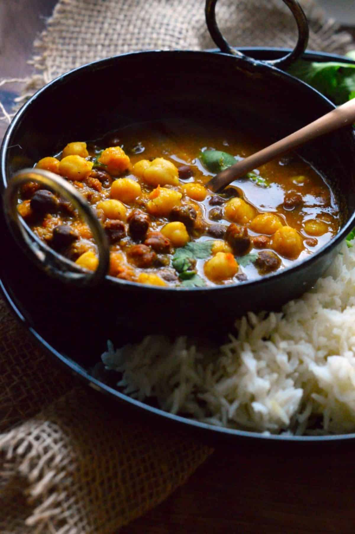 Mixed Chickpeas Curry in a black bowl with a spoon.