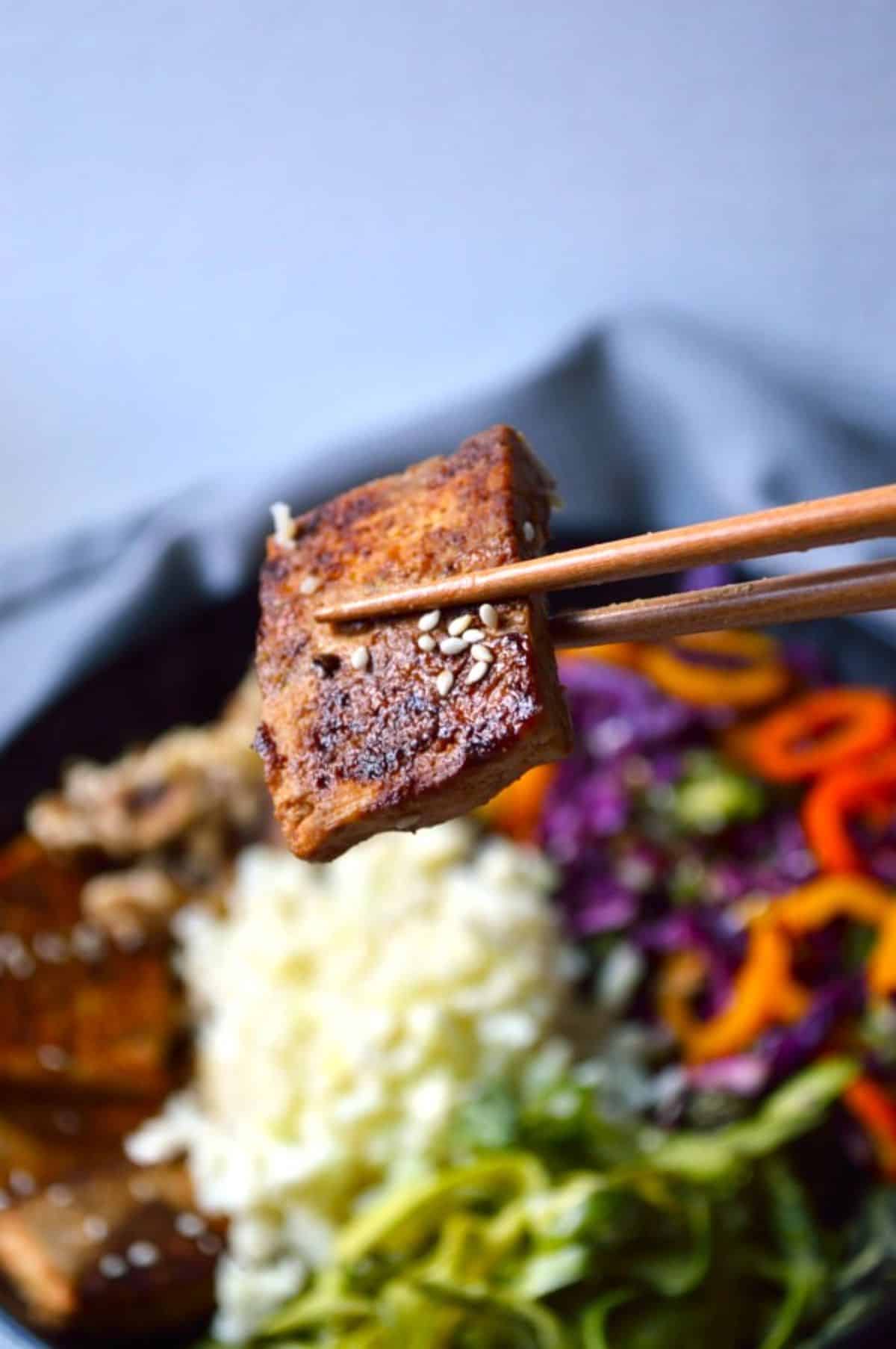 Pan-Fried Sesame Garlic Tofu held by chopsticks.