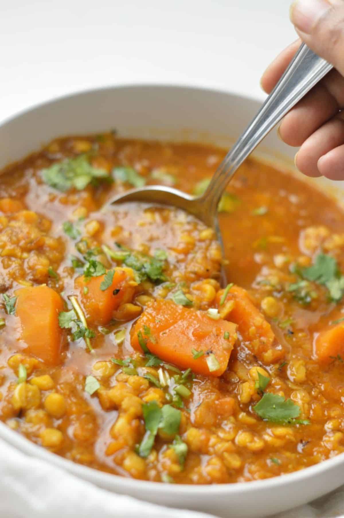 Pumpkin Chana Dal in a white bowl scooped by a spoon.