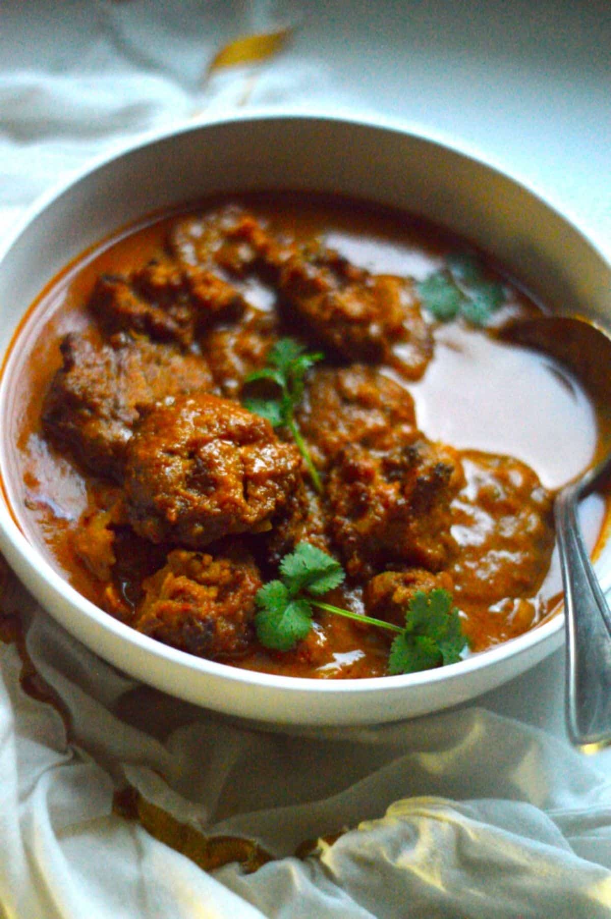 Vada Curry dish in a white bowl with a spoon.