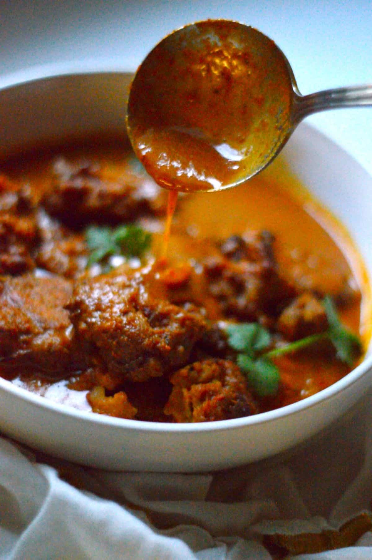 Vada Curry dish in a white bowl with a spoon.