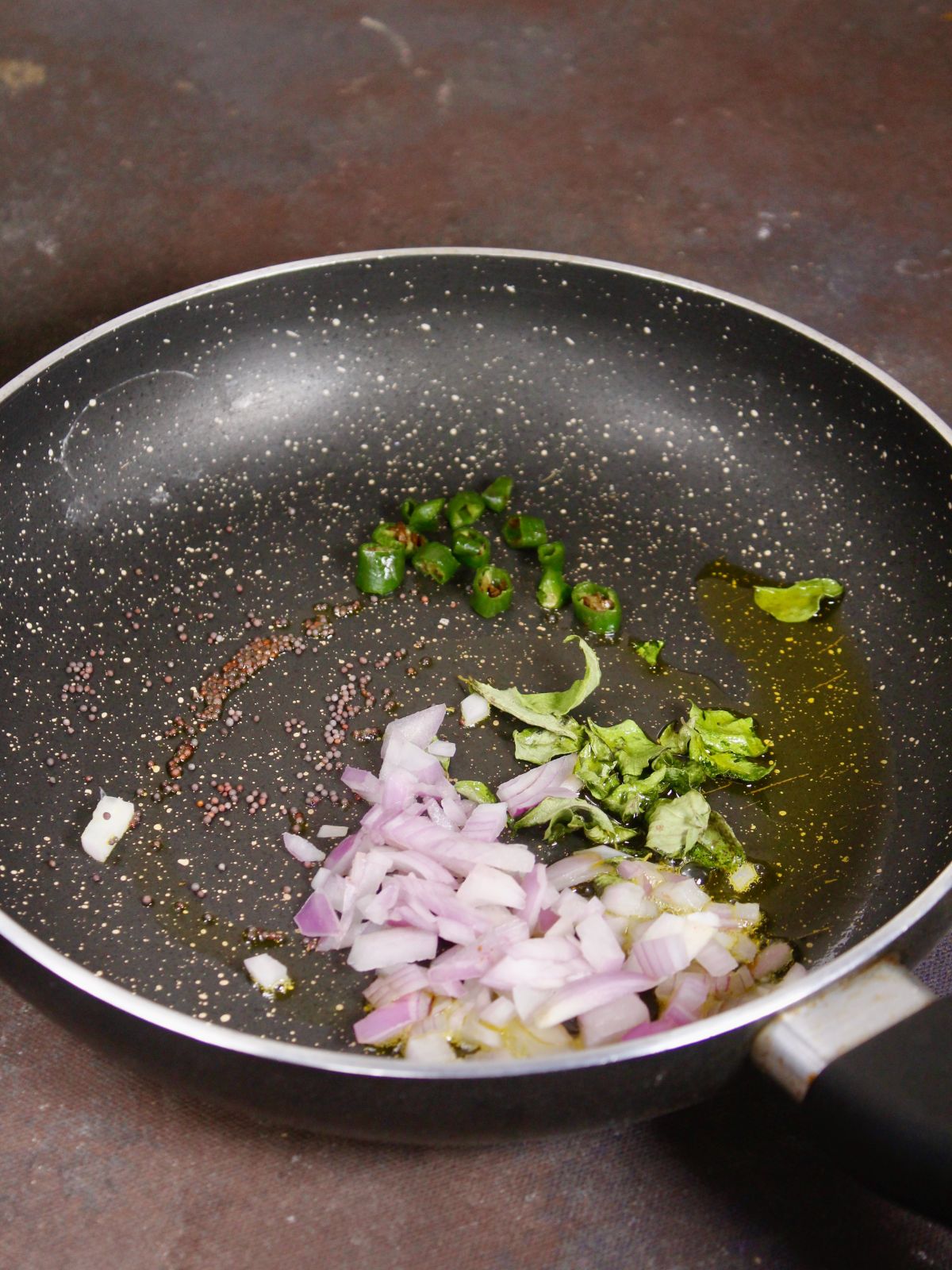 add seeds, green chilies, curry leaves, and chopped onions in a pan 