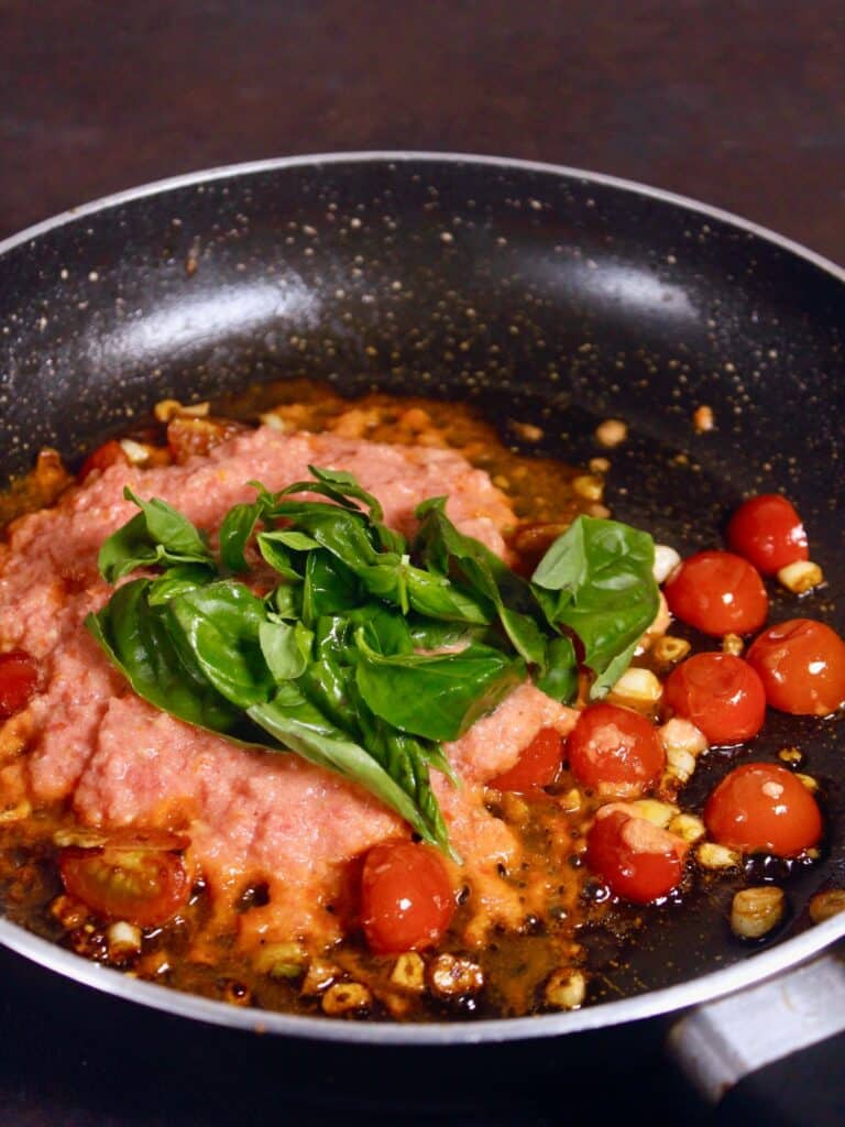 add tomato puree and basil leaves to the mixture 